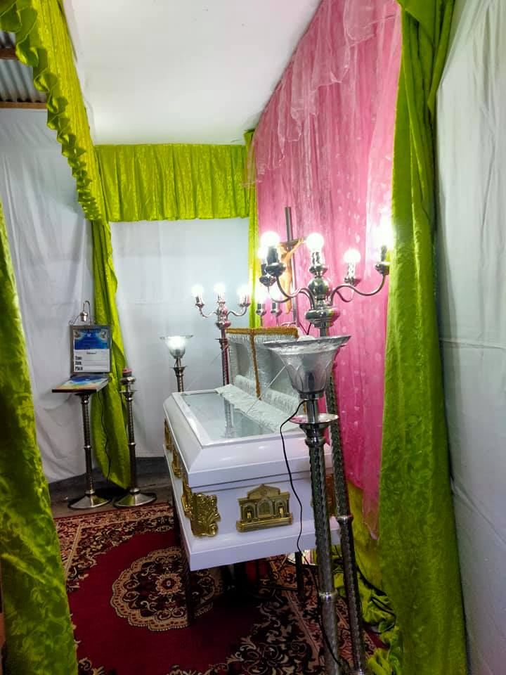Home wake with green and pink drapes, candelabras and a white casket