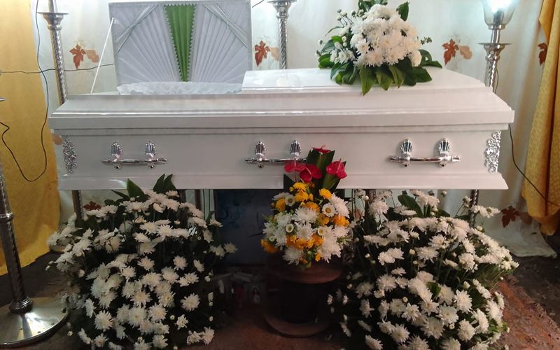 White casket with flower arrangements at a home wake